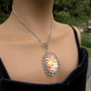 Necklace Pendant with decorative cream colored holiday bells on red background and silver frame being worn by model