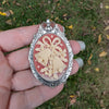 Festive Pendant and Brooch combo with decorative cream colored holiday bells on red background and silver frame in a hand