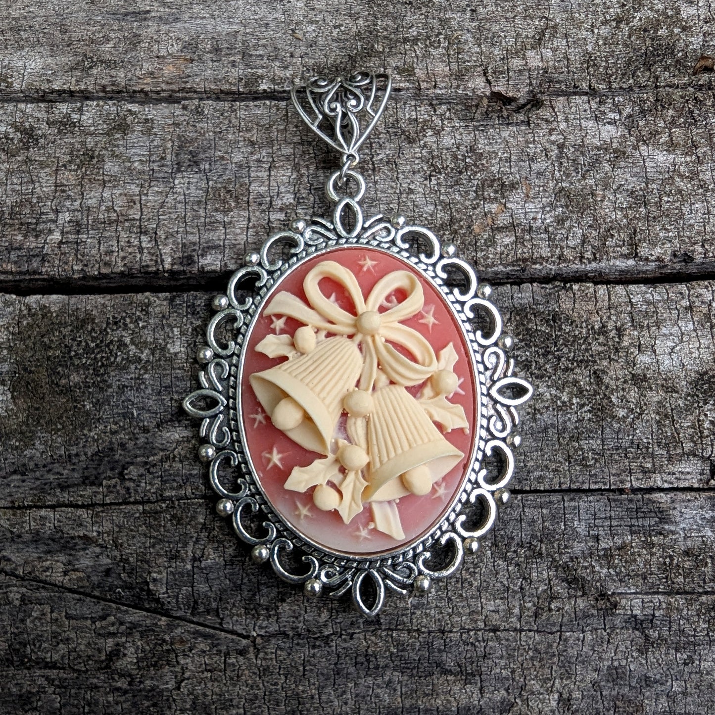 Necklace Pendant with decorative cream colored holiday bells on red background and silver frame on wood surface