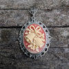 Necklace Pendant with decorative cream colored holiday bells on red background and silver frame on wood surface