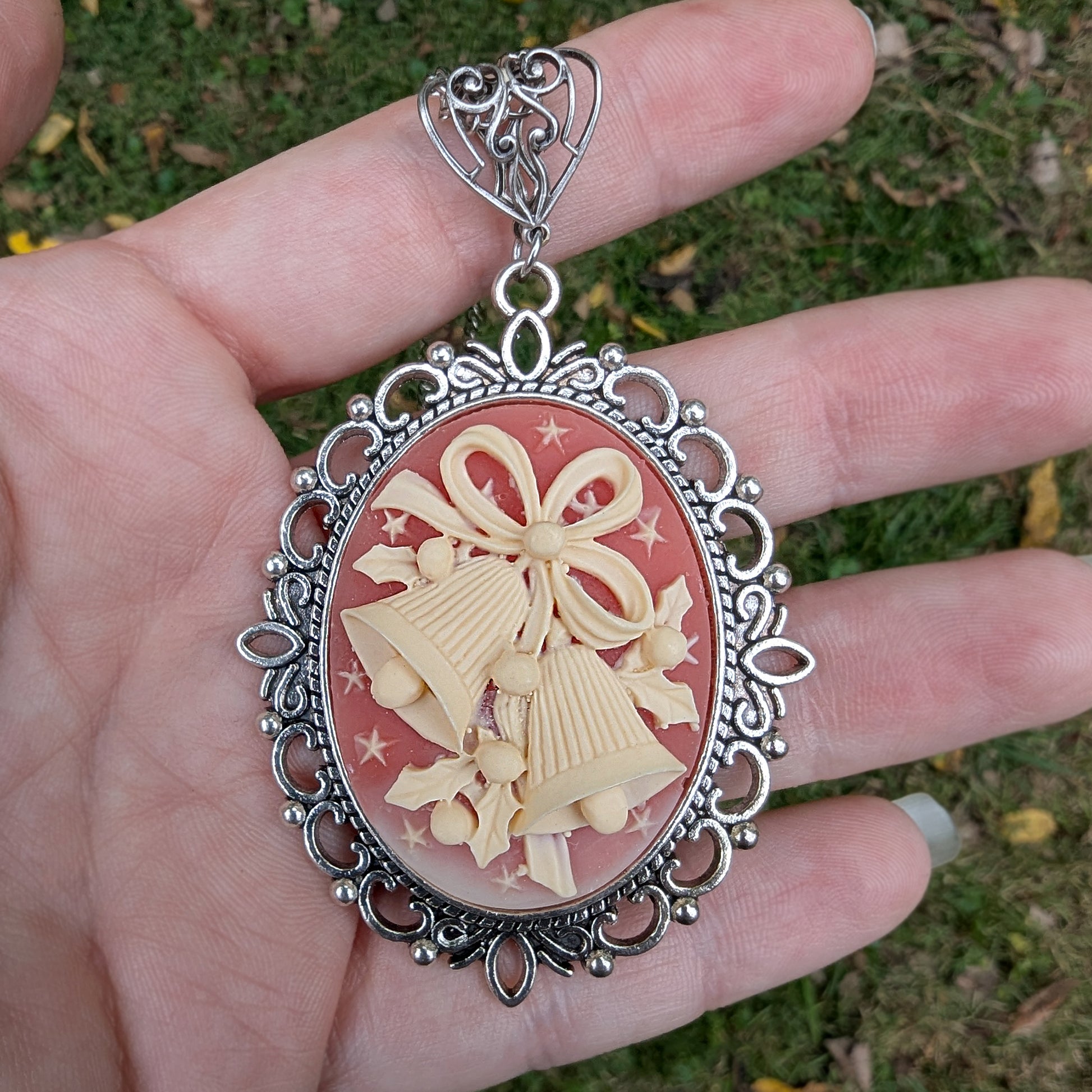 Necklace Pendant with decorative cream colored holiday bells on red background and silver frame being held in a hand