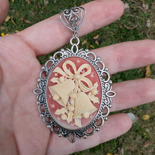 Necklace Pendant with decorative cream colored holiday bells on red background and silver frame being held in a hand