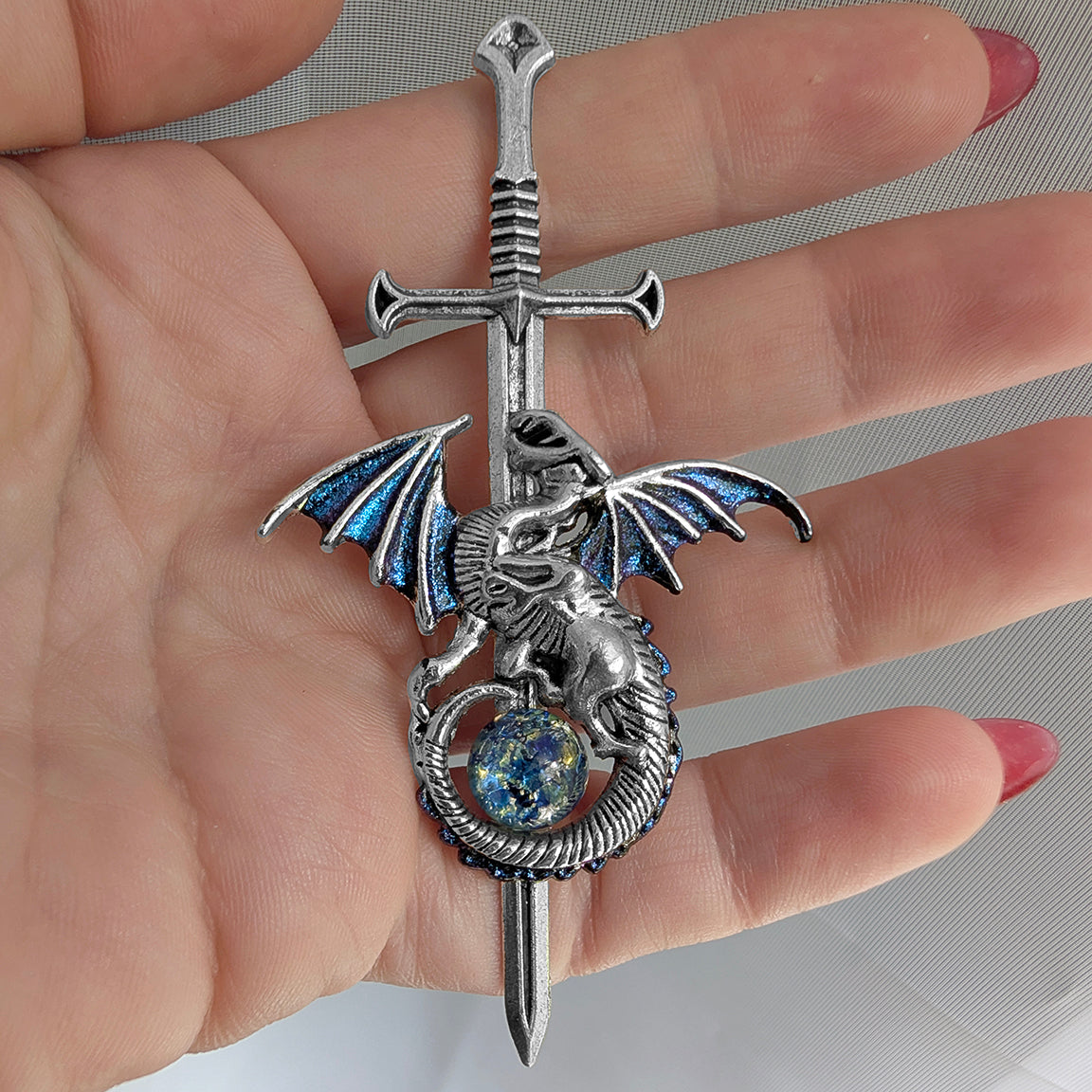 Silver dragon pendant with a sword on a hand against a neutral background