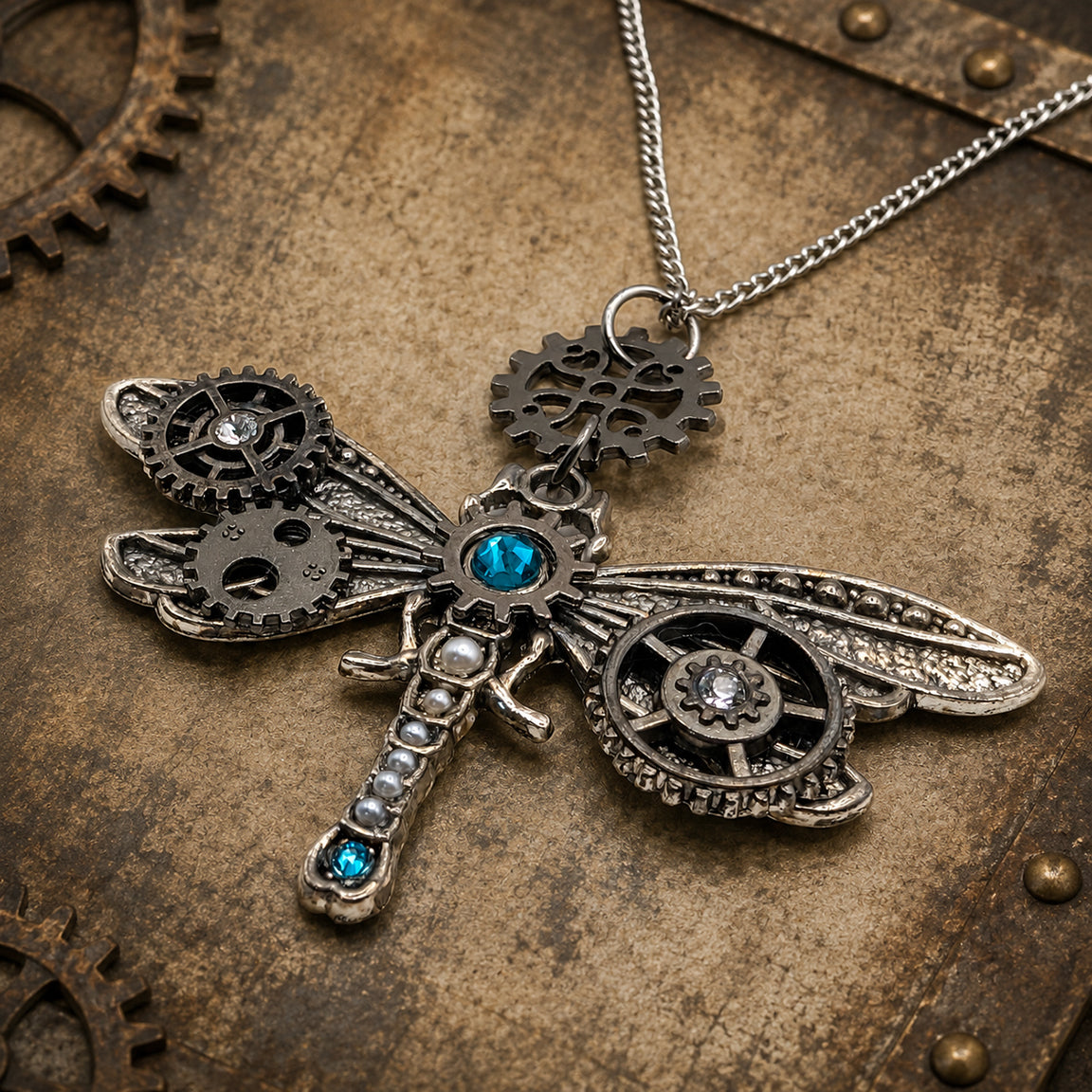 Steampunk dragonfly pendant necklace with intricate metal gears, clear and blue crystal accents, displayed on a textured vintage metal background.