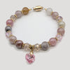 Beaded bracelet with pink heart charm on a light gray background