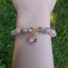 Bracelet with heart-shaped pink charm on a wrist against a grass background