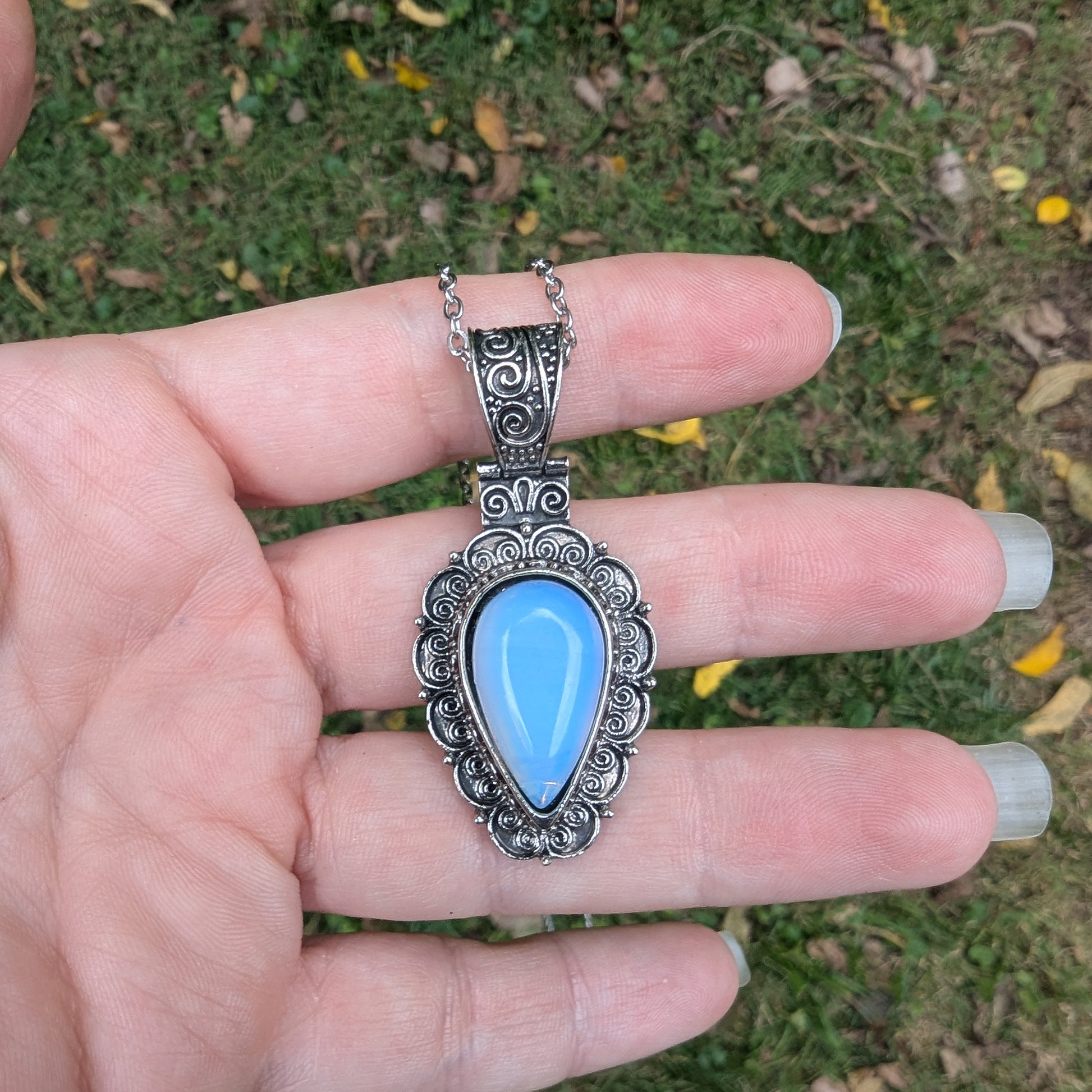 Silver pendant with a blue stone held in a hand against a natural background