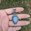 Silver pendant with a blue stone held in a hand against a natural background