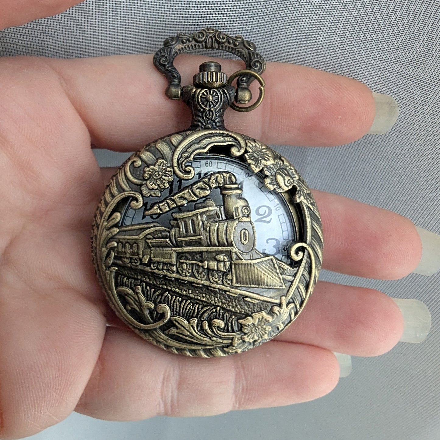 Bronze pocket watch with train design held in a hand against a gray background