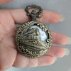 Bronze pocket watch with train design held in a hand against a gray background