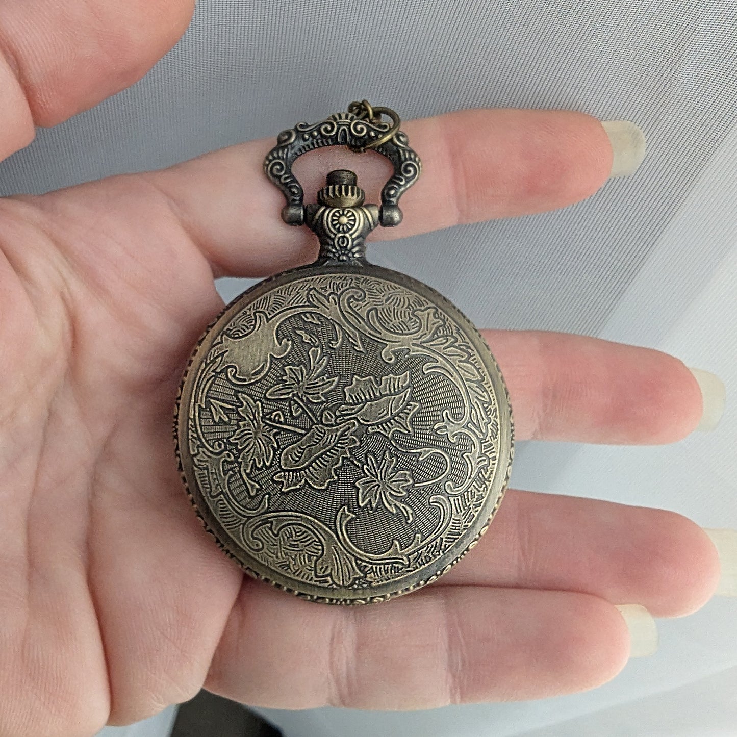 Hand holding a decorative pocket watch with intricate designs on a plain background