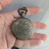 Hand holding a decorative pocket watch with intricate designs on a plain background