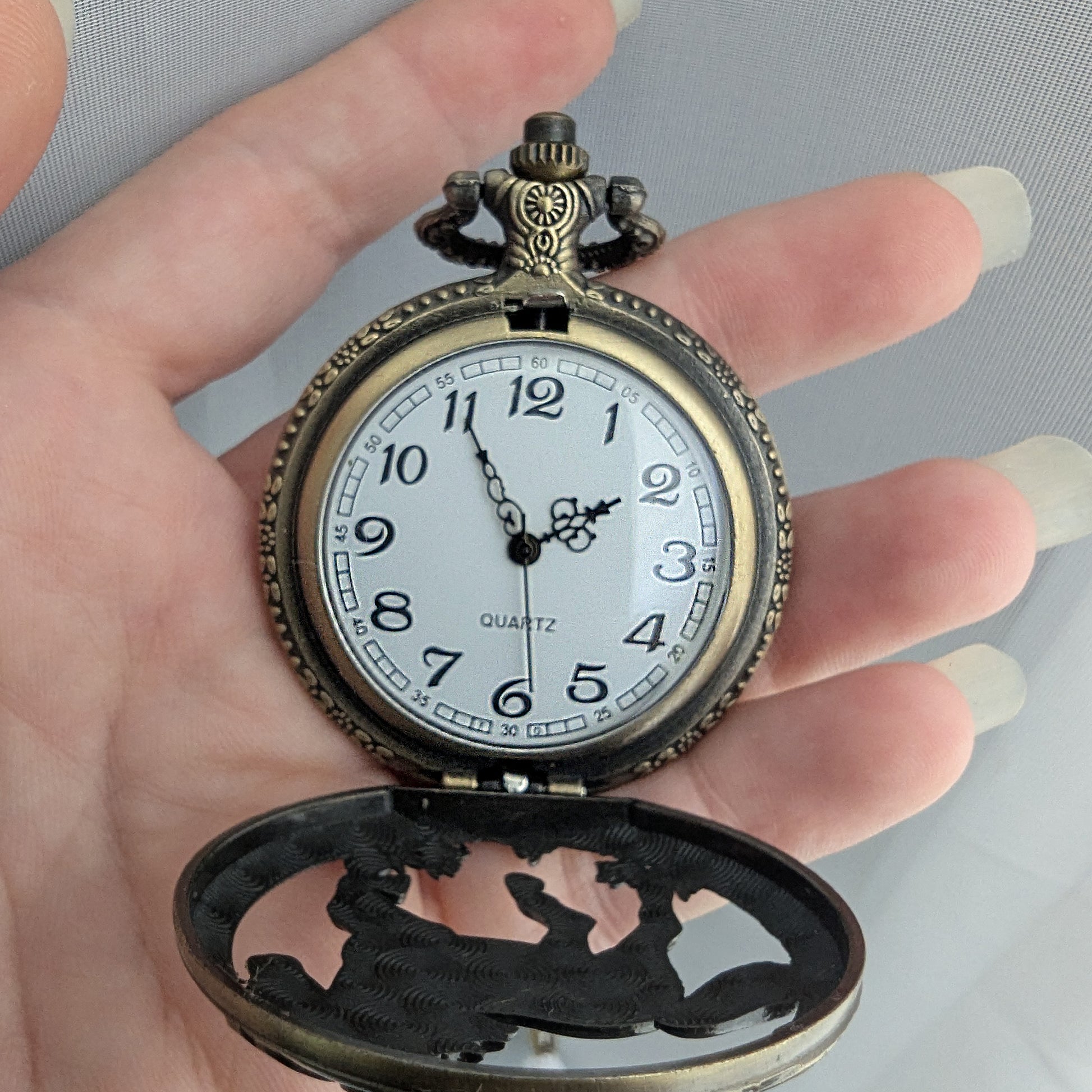 Vintage pocket watch held in a hand with a plain background
