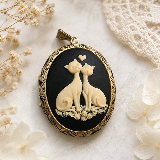 Antique Gold-framed locket pendant with two cats and a heart on a black background, surrounded by white flowers and lace.