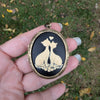 cream and black colored cat lovers cameo locket necklace displayed in hand outdoors.