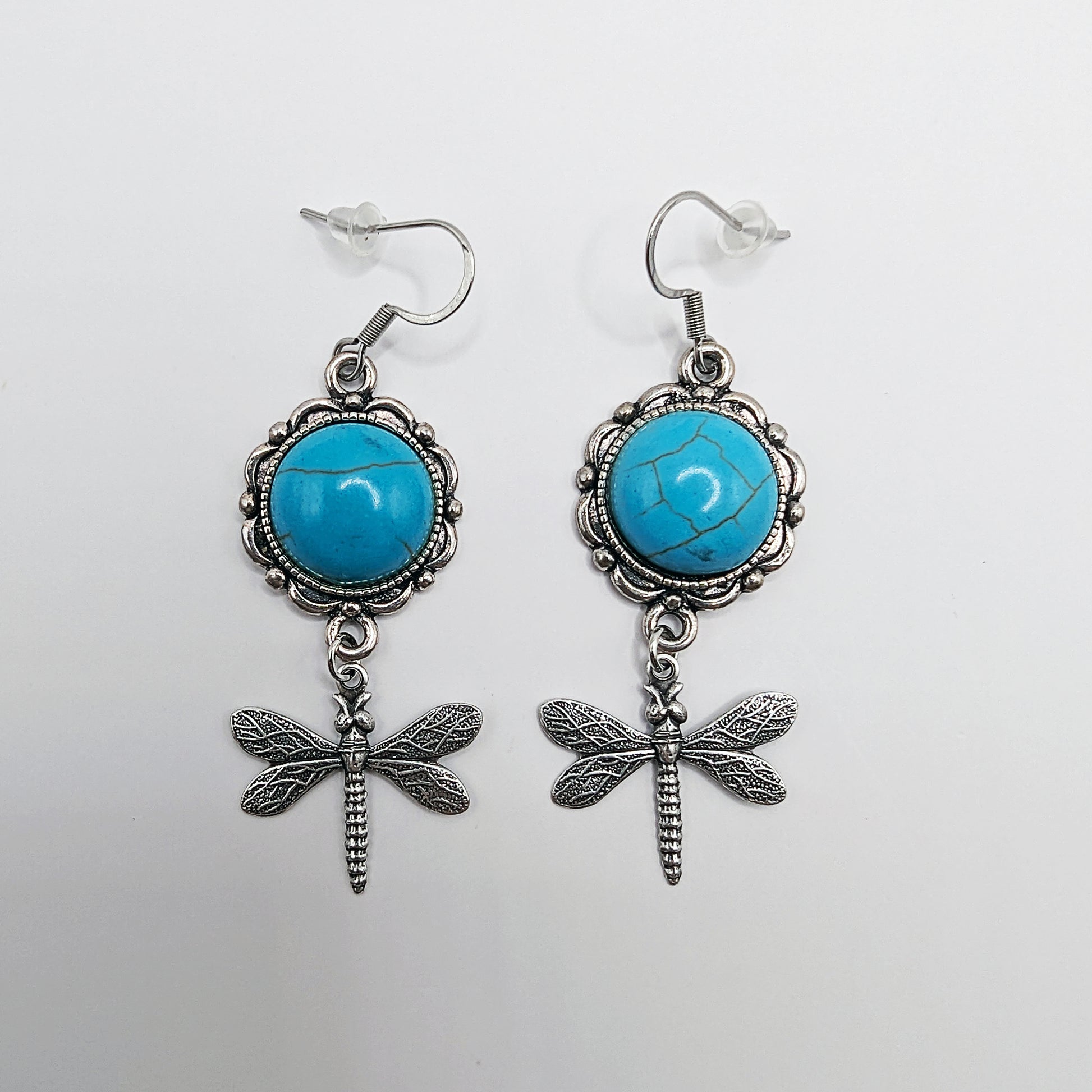 Pair of earrings with turquoise stones and dragonfly designs on a white background