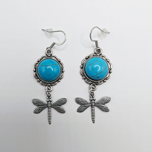 Pair of earrings with turquoise stones and dragonfly designs on a white background
