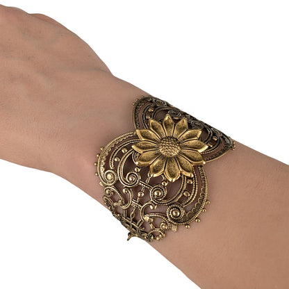 Vintage style brass floral sunflower statement bracelet on a wrist against white background