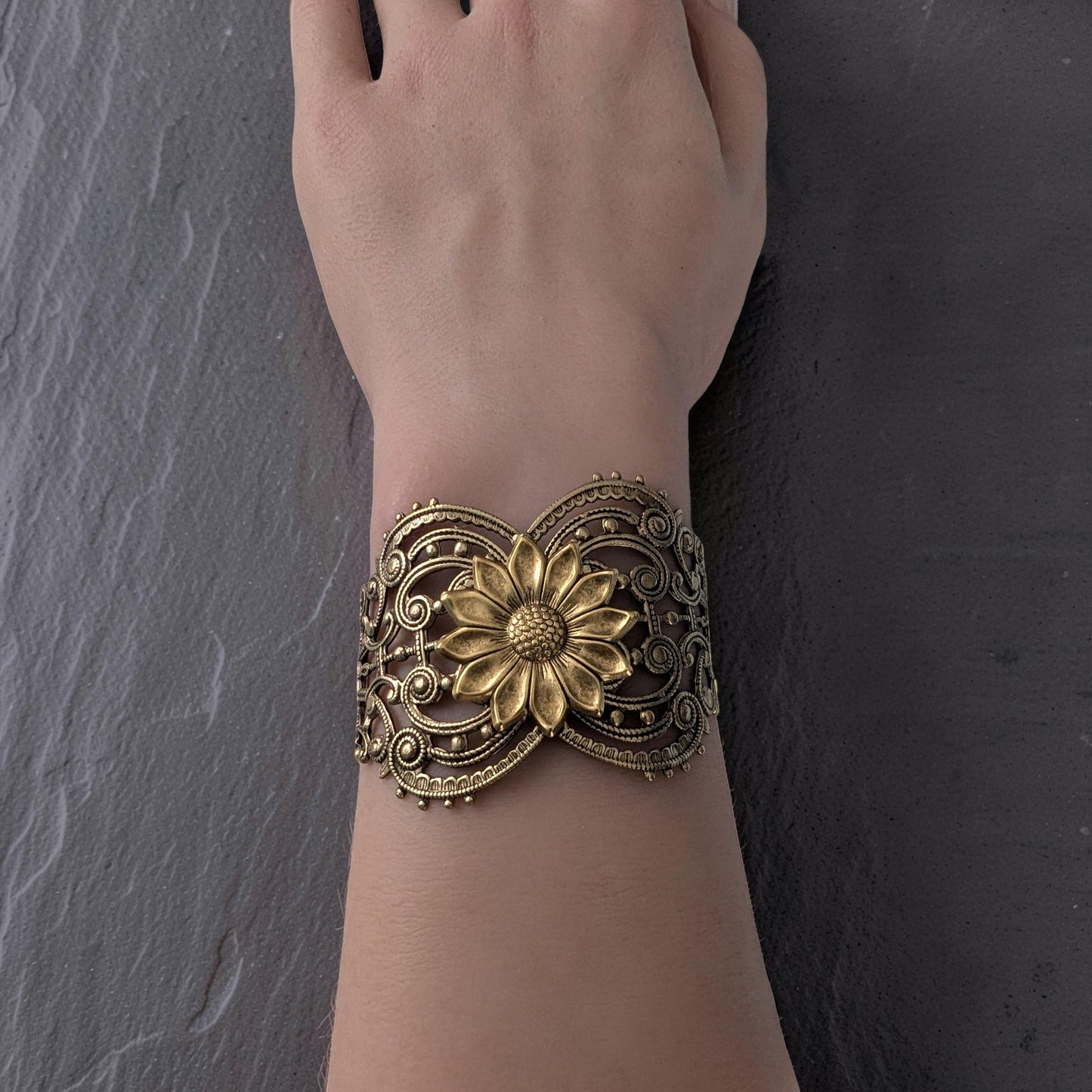 Vintage style brass floral sunflower statement bracelet on a wrist against a dark background