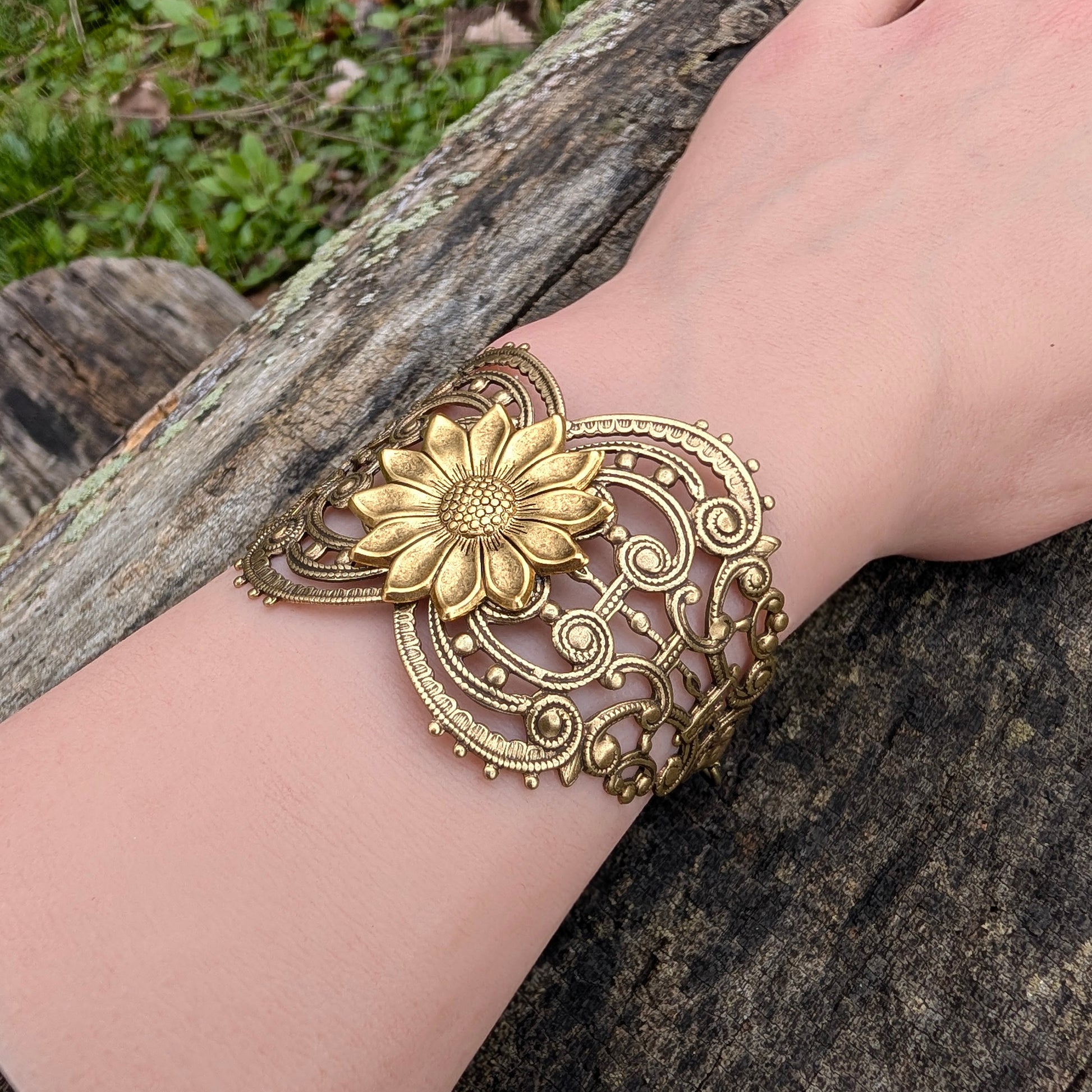 Vintage style brass floral sunflower statement bracelet on a wrist with natural background