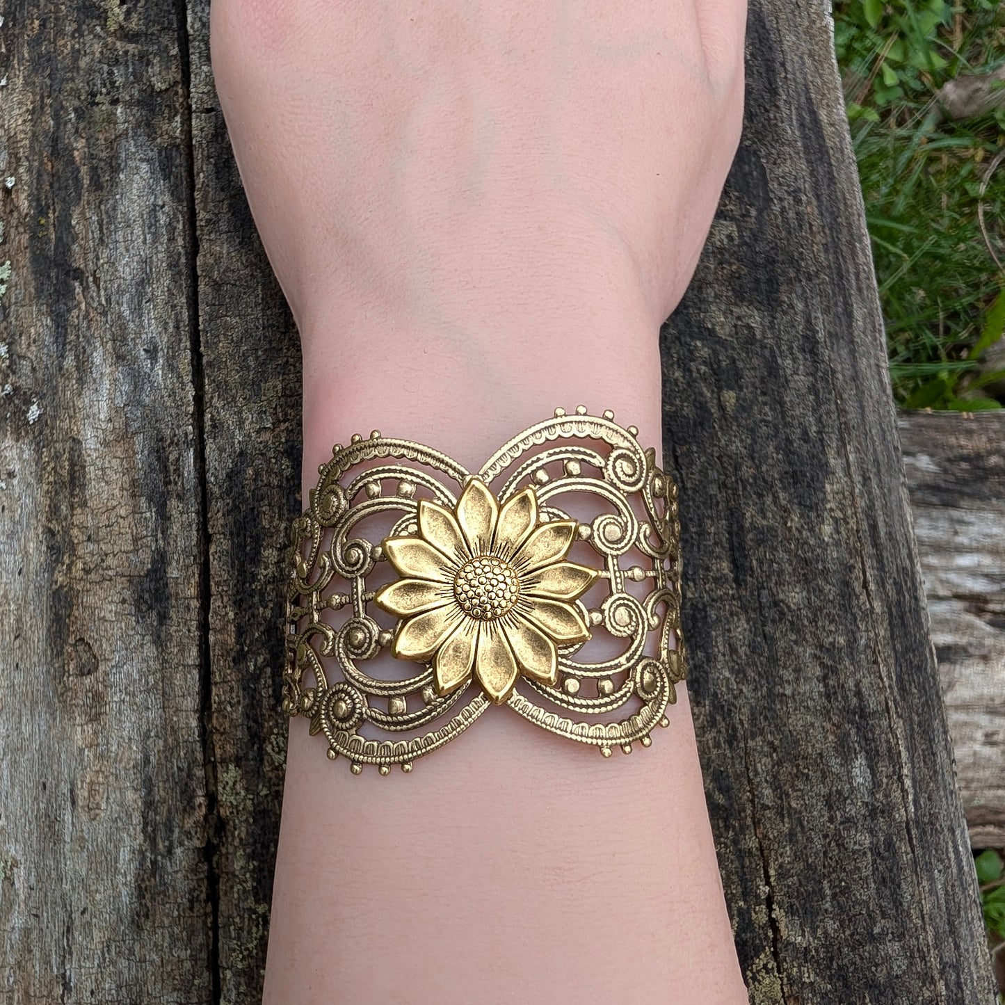 Vintage style brass floral sunflower statement bracelet on a wrist with log background