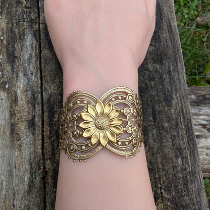 Vintage style brass floral sunflower statement bracelet on a wrist with log background