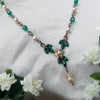 Vintage Art Deco Swarovski Emerald crystal and pearl floral necklace on a white fabric background with flowers.