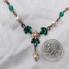Vintage Art Deco Swarovski Emerald crystal and pearl floral necklace next to a quarter for scale on a light gray background