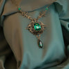 Ornate necklace with green gemstones on a teal fabric background