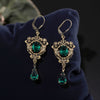 Baroque-inspired earrings with dangling green Swarovski teardrop and antique gold finish
