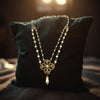 Pearl necklace with a gold chain and pendant on a dark pillow