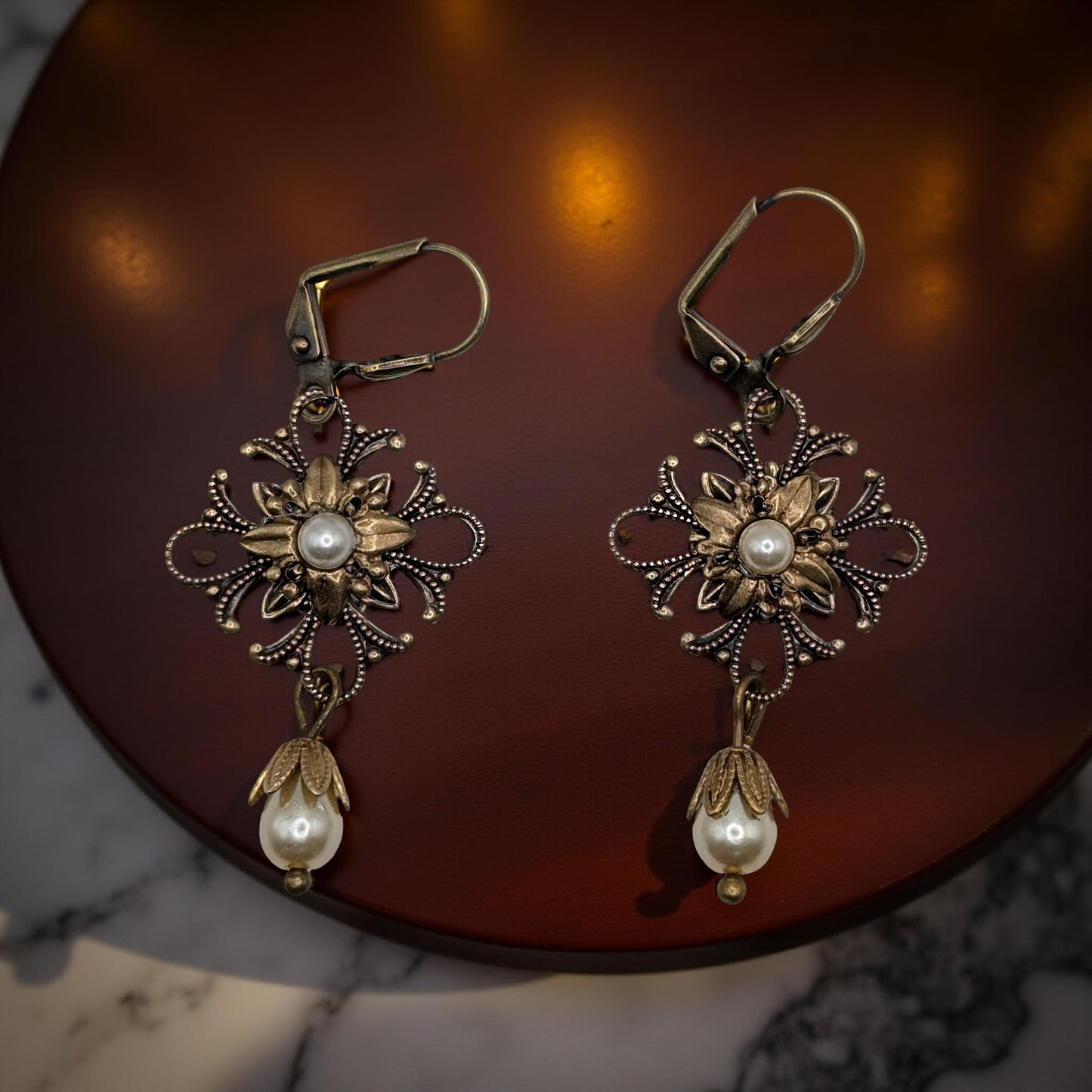 Pair of ornate earrings with pearl drops on a dark surface
