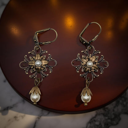 Pair of ornate earrings with pearl drops on a dark surface