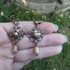 Pair of ornate gold earrings held in a hand with a natural background
