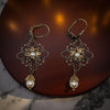 Pair of ornate earrings with pearl drops on a dark surface