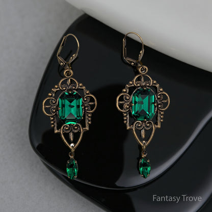 Ornate earrings with green gemstones on a reflective surface, branded 'Fantasy Trove'.