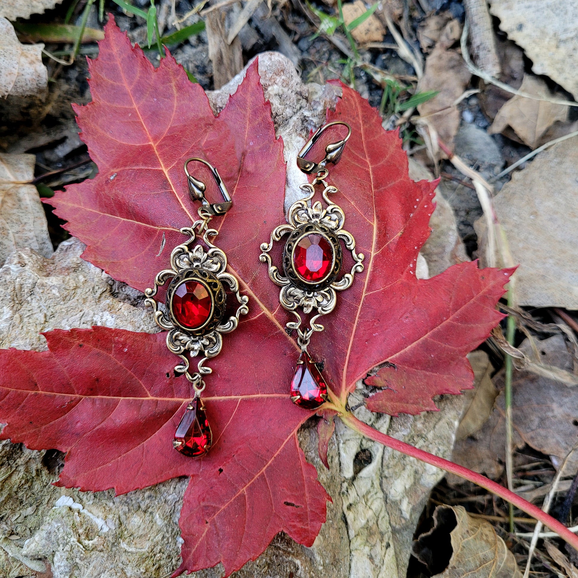 A pair of vintage styled red Swarovski crystal earrings laying on a red leaf outdoors.