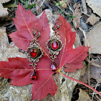 A pair of vintage styled red Swarovski crystal earrings laying on a red leaf outdoors.