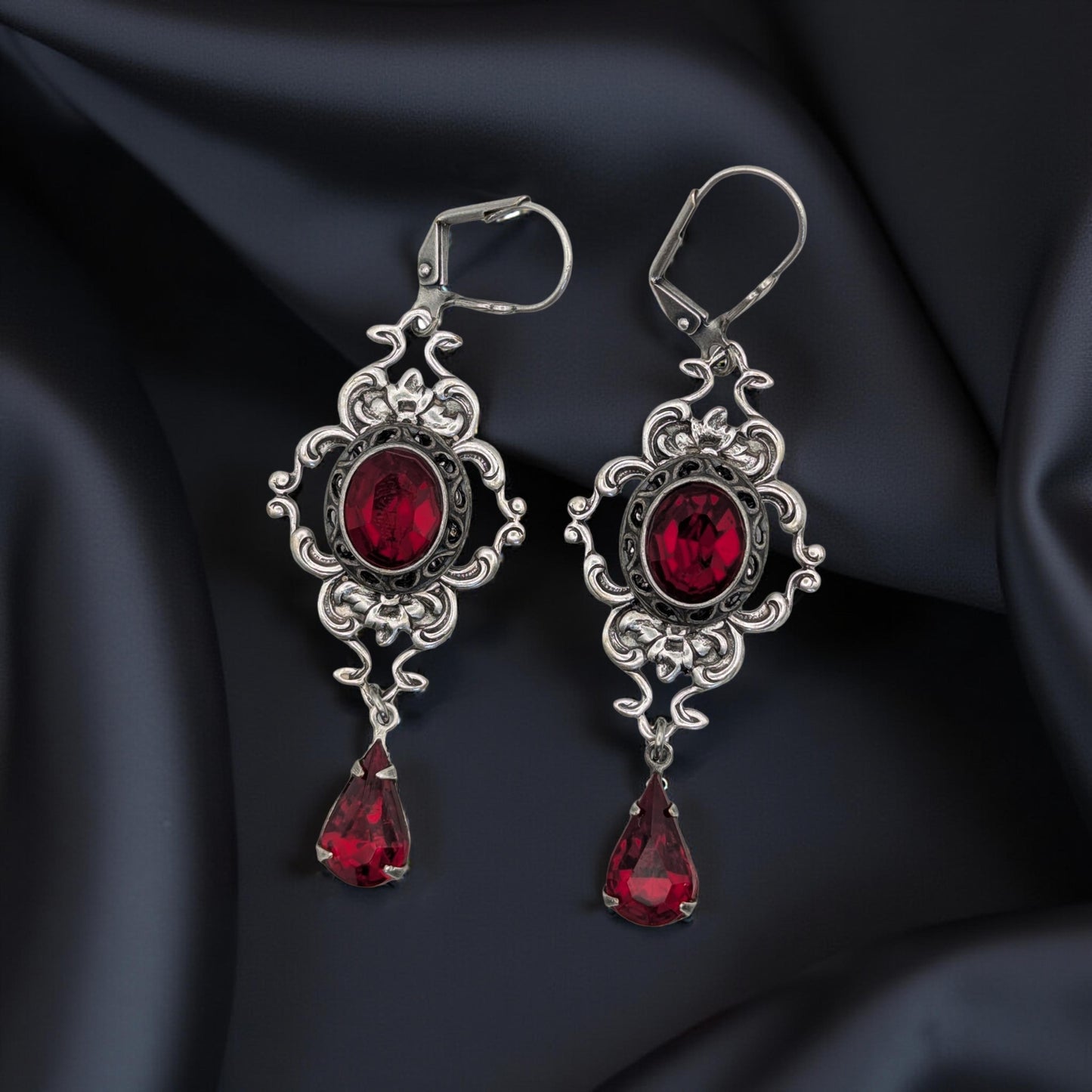 A pair of vintage styled red Swarovski crystal earrings laying on a bloack surface