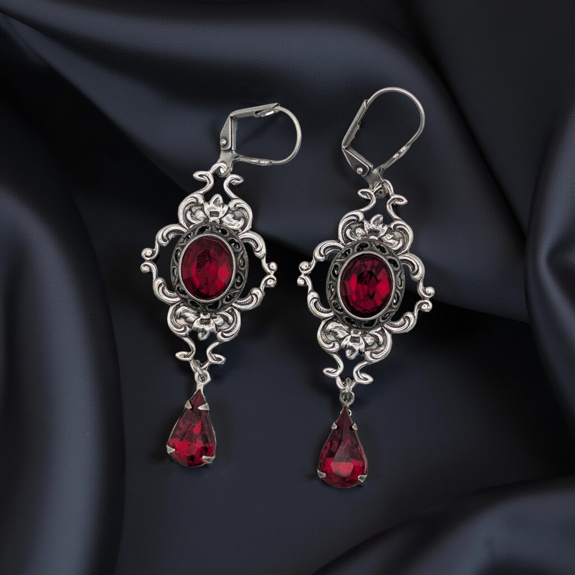 A pair of vintage styled red Swarovski crystal earrings laying on a bloack surface