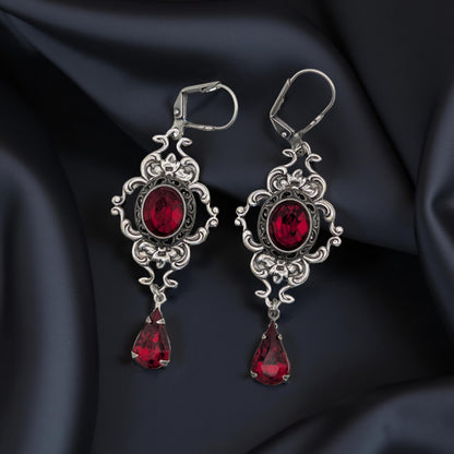 A pair of vintage styled red Swarovski crystal earrings laying on a bloack surface