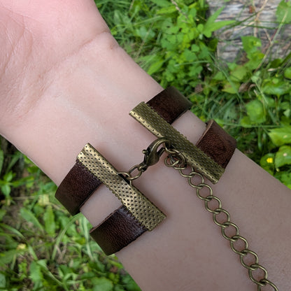 Bracelet with brown leather straps and gold chain on a wrist against a natural background
