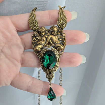 Detailed view of brass cherub pendant with emerald Swarovski crystal centerpiece and teardrop accent