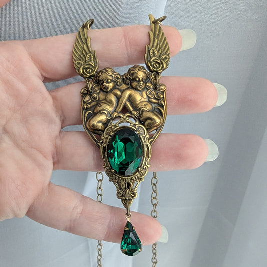 Detailed view of brass cherub pendant with emerald Swarovski crystal centerpiece and teardrop accent