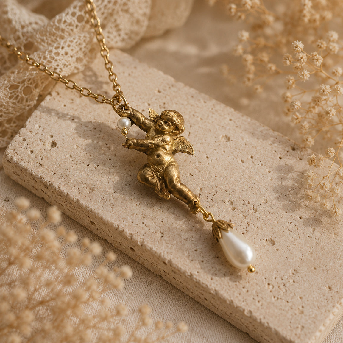 Brass necklace with cherub pendant and pearl drop on a textured beige surface.  Angel necklace
