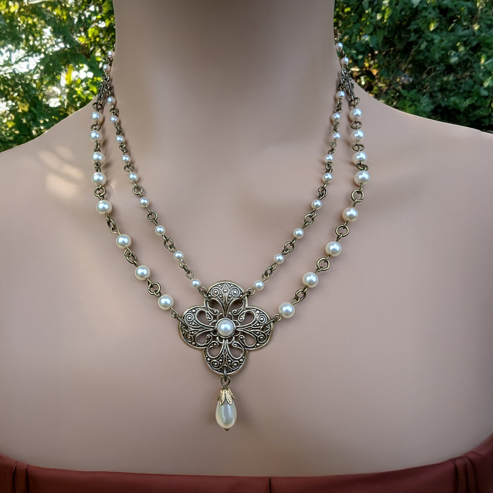 Necklace with floral pendant and pearl beads on a woman against a blurred green background
