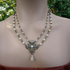 Necklace with floral pendant and pearl beads on a woman against a blurred green background