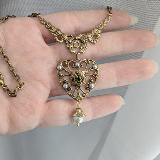 Gold heart-shaped necklace with intricate designs held in a hand against a neutral background