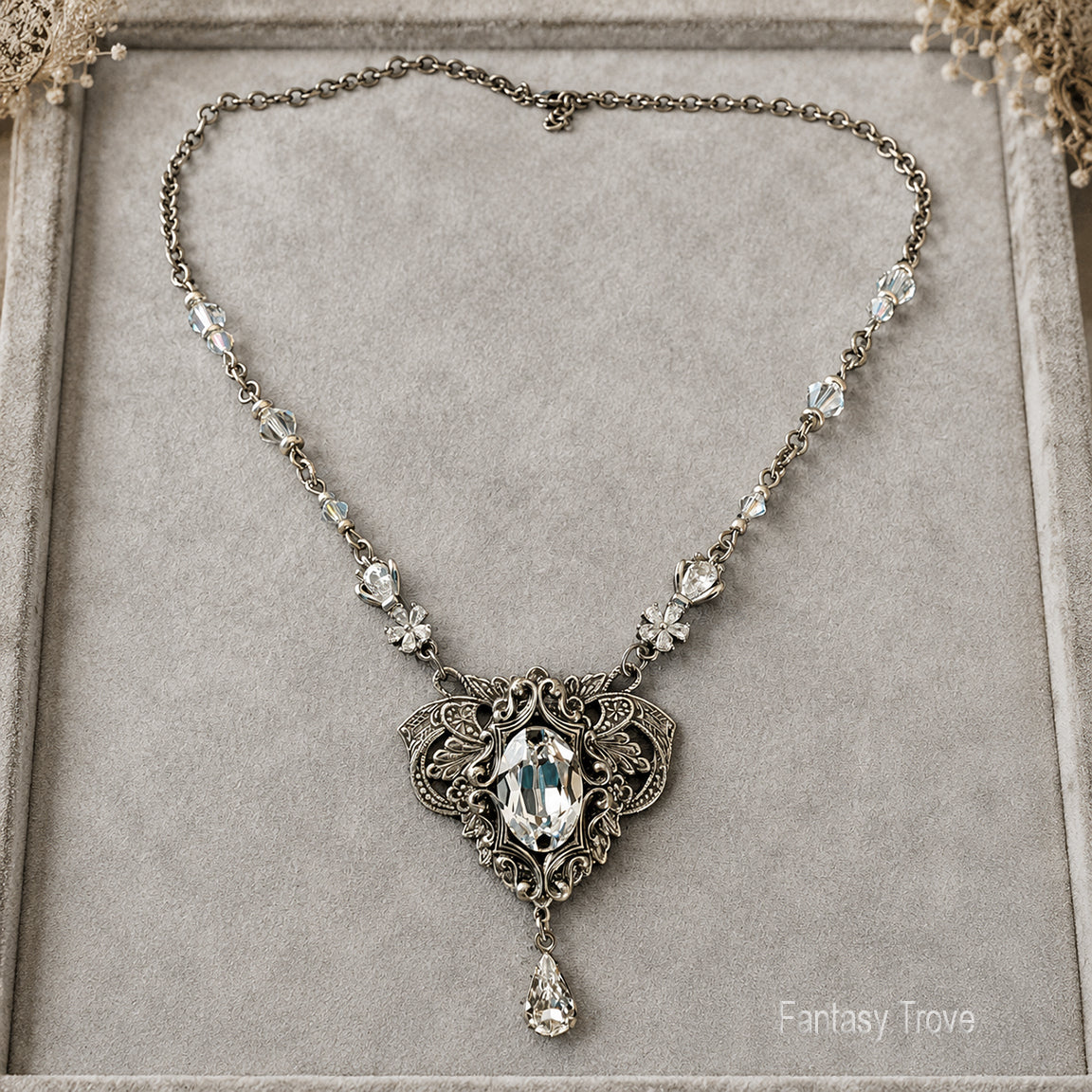 An ornate elven-style necklace with a vintage silver filigree pendant featuring a large marquise-cut Swarovski crystal and smaller clear crystals along the chain, displayed on a gray velvet jewelry box.  Fantasy princess bridal jewelry.