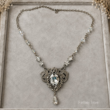 An ornate elven-style necklace with a vintage silver filigree pendant featuring a large marquise-cut Swarovski crystal and smaller clear crystals along the chain, displayed on a gray velvet jewelry box.  Fantasy princess bridal jewelry.